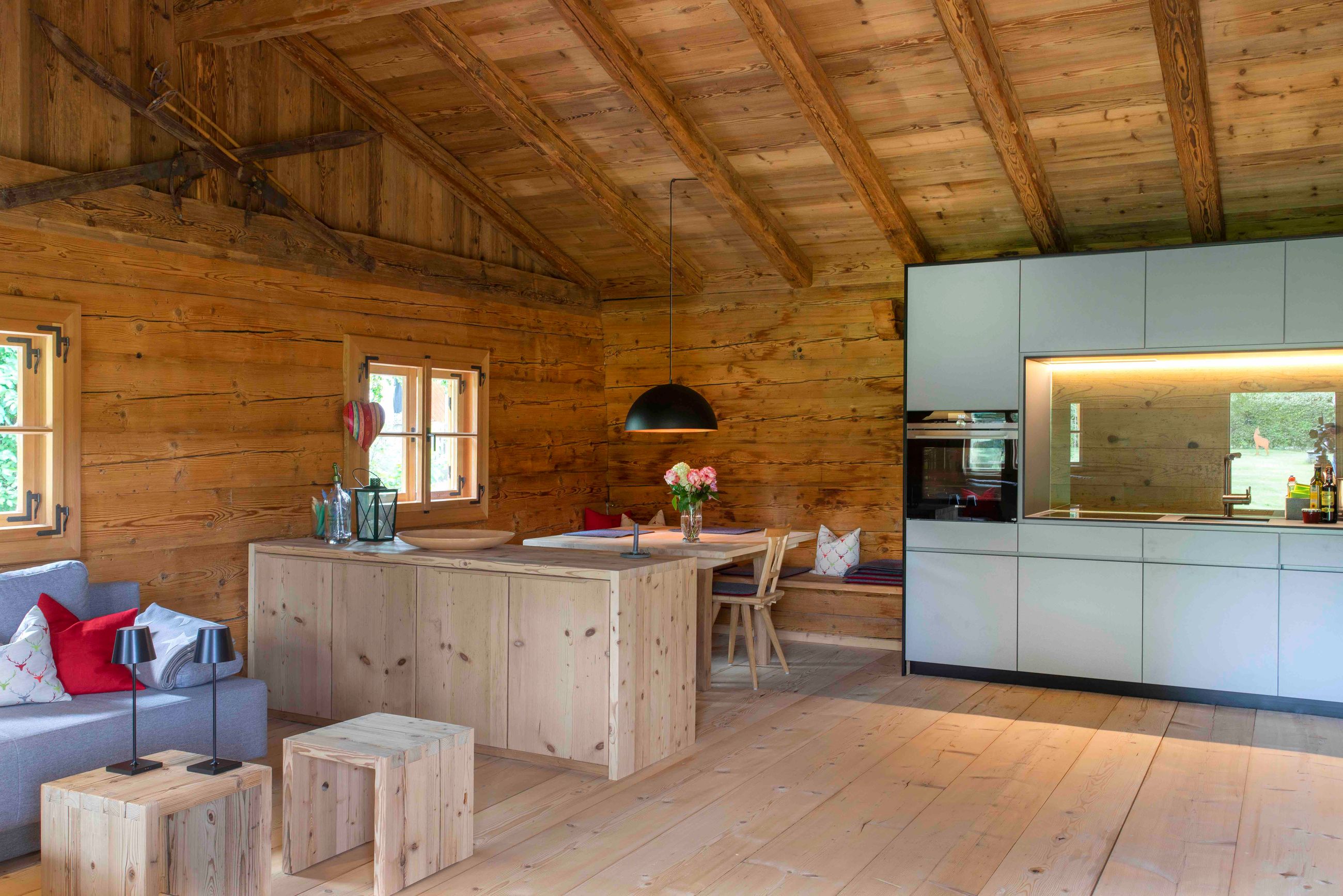 Gemütliches Interieur einer Holzhütte mit moderner Küche, Essbereich, Sofa mit roten und weißen Kissen