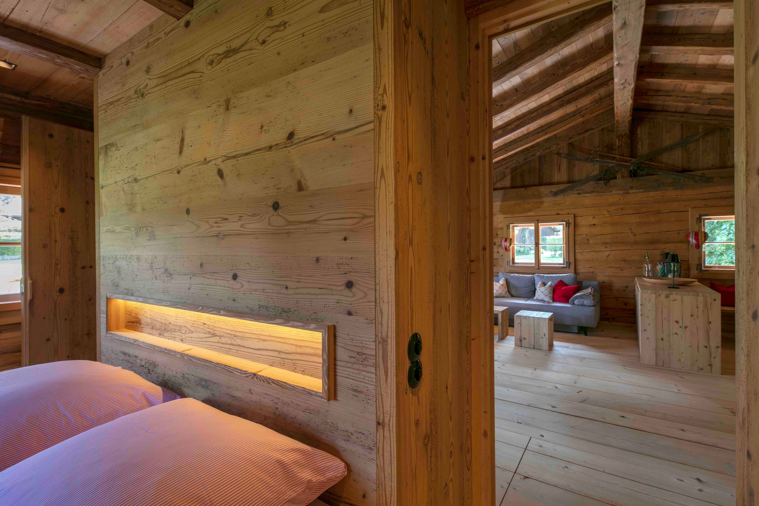 Rustikales Holzinterieur mit einem Schlafzimmer mit zwei Betten und einem separaten Wohnbereich mit einem grauen Sofa und Holzmöbeln unter einer gewölbten Decke.