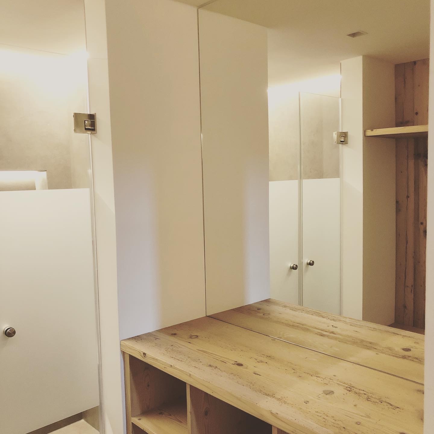 Minimalistisches Badezimmer mit Duschkabinentüren aus Milchglas, einem Waschtisch aus Holz mit offenen Regalen und großen Spiegeln.